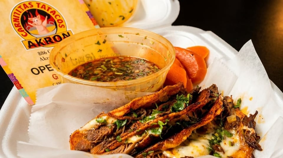 Three cheesy birria tacos with cilantro, a side of consommé, and pickled carrots in a takeout container.