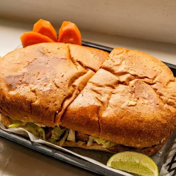 A large torta sandwich in a black basket with a lime wedge and papaya slices.