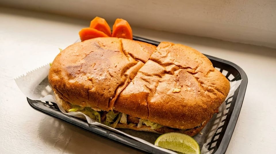 A large torta sandwich in a black basket with a lime wedge and papaya slices.